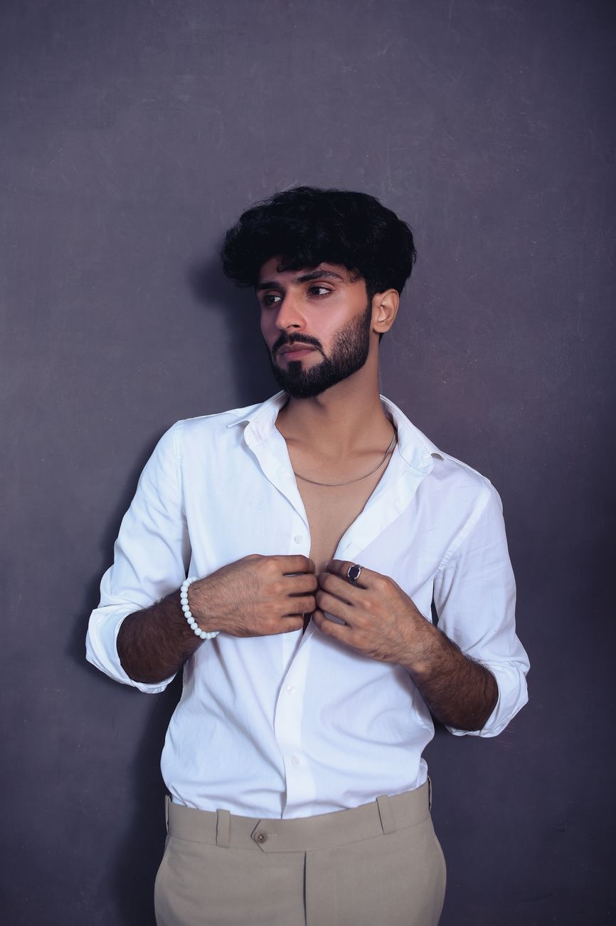 A fashionable young man poses in a white shirt, exuding confidence and style.
