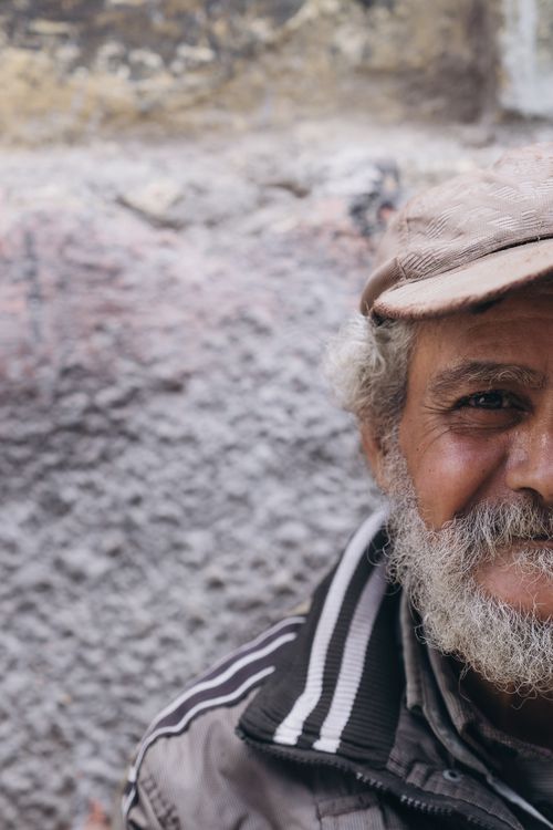 Free Close-up portrait of a smiling elderly man wearing a cap against a textured wall background. Stock Photo