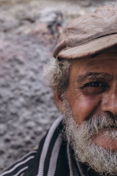 A close-up portrait of a smiling elderly man with a beard and cap in Alexandria, Egypt.