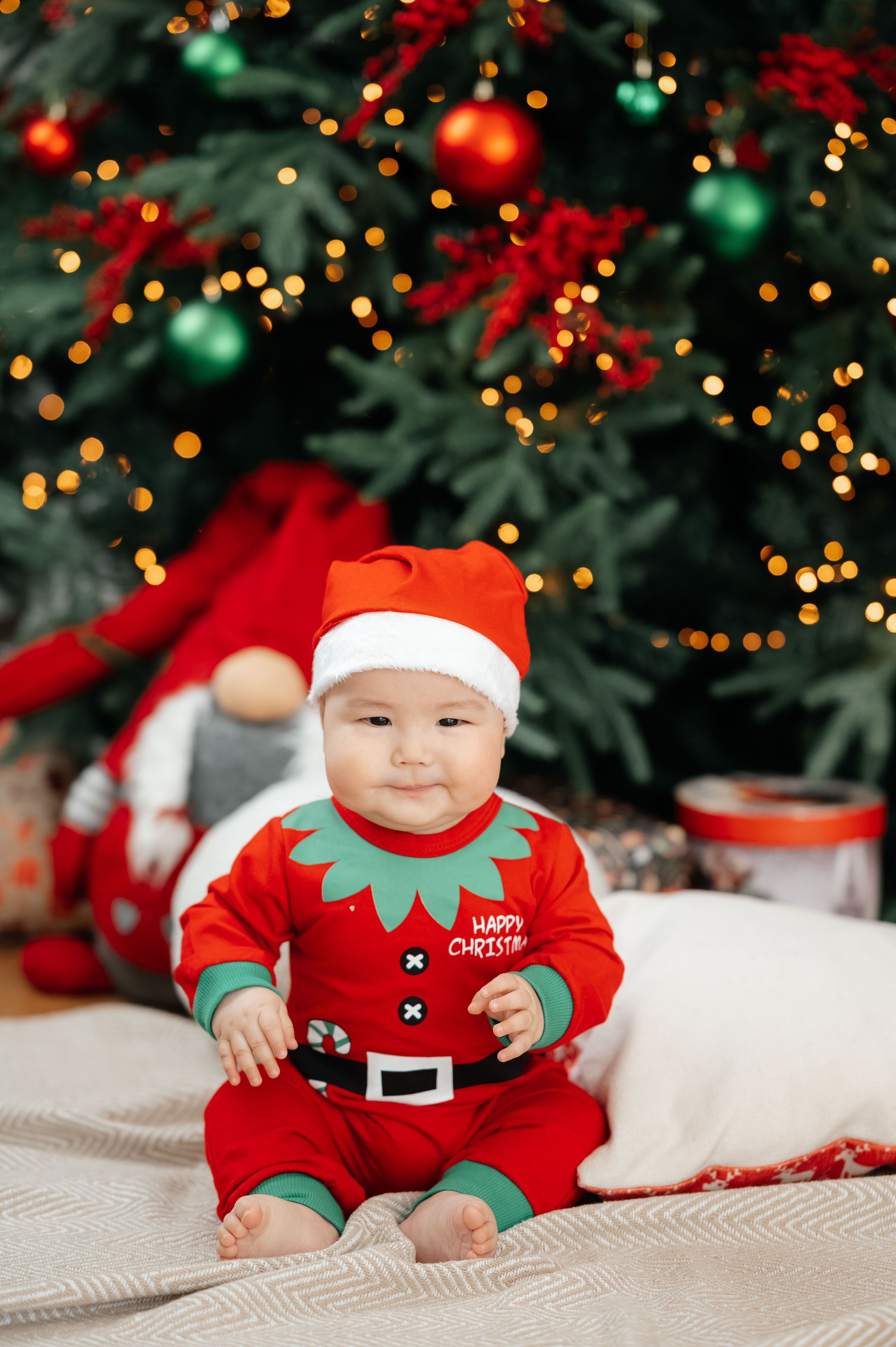 Cute baby in Santa outfit with Christmas tree backdrop