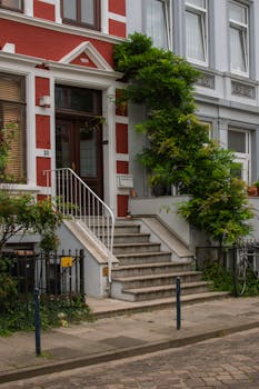 A street view of an elegant red brick home facade adorned with lush greenery and steps.