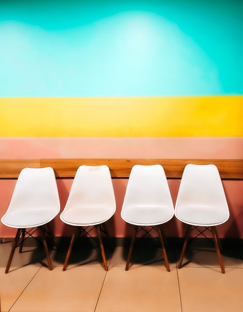 Free Four contemporary chairs against a vibrant, multicolored wall, showcasing minimalist design. Stock Photo