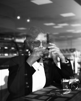 Stylish adult enjoying coffee in cafe with retro camera, captured in monochrome.