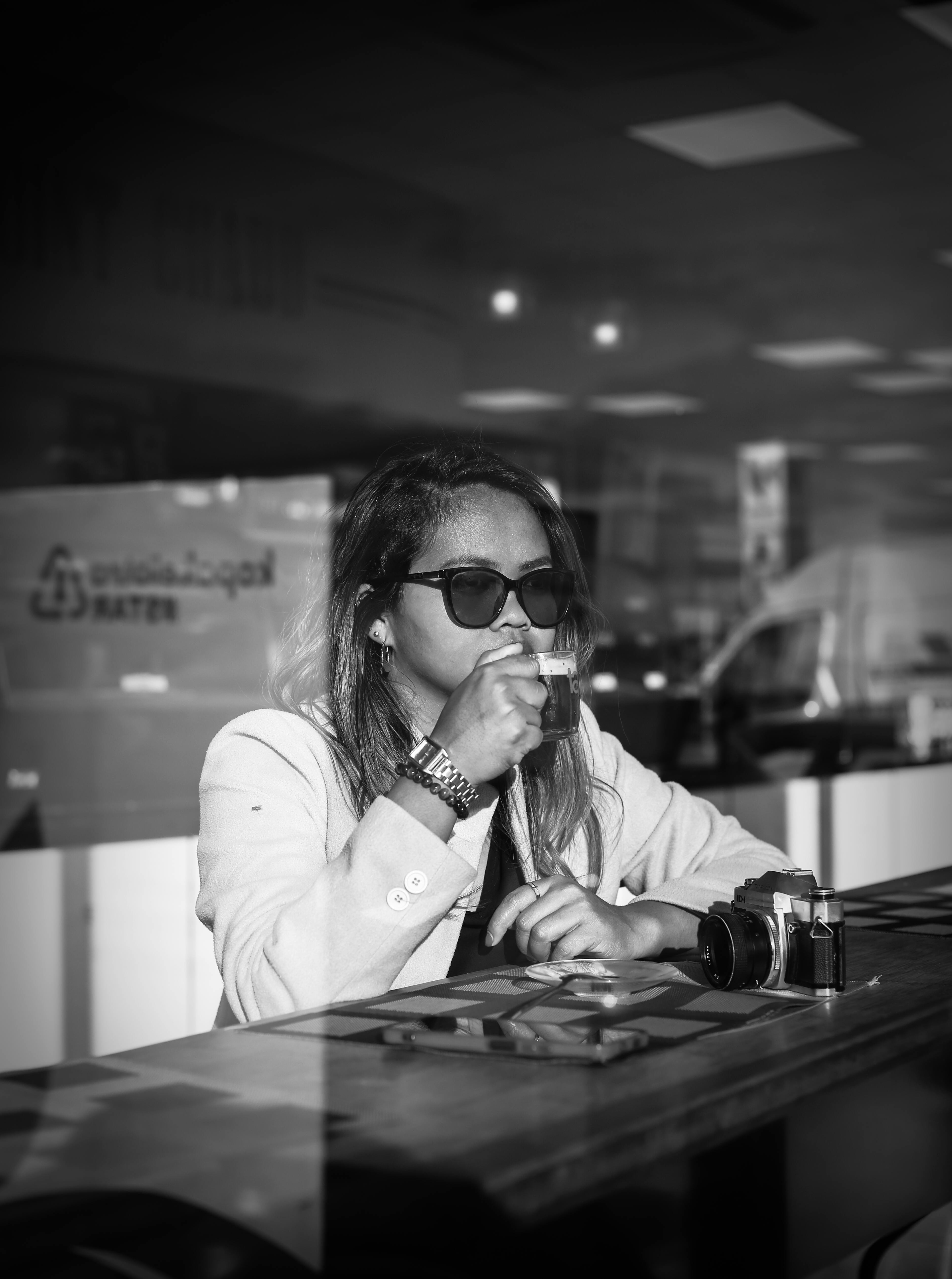 Elegant woman in sunglasses sipping coffee in a modern cafe setting.