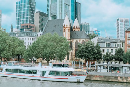 Frankfurt cityscape featuring a historic church, modern skyscrapers, and a boat along the river.