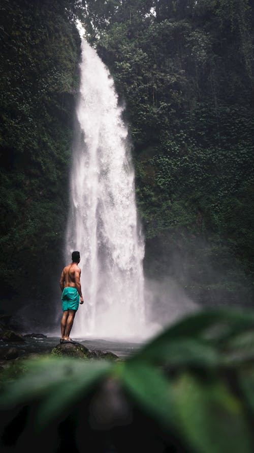 Photo of a Topless Man Standing on a Rock Near a Waterfall