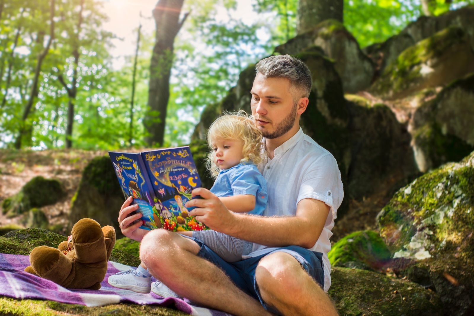 Un adulto e un bambino leggono insieme un libro all'aperto, immersi nella luce del bosco