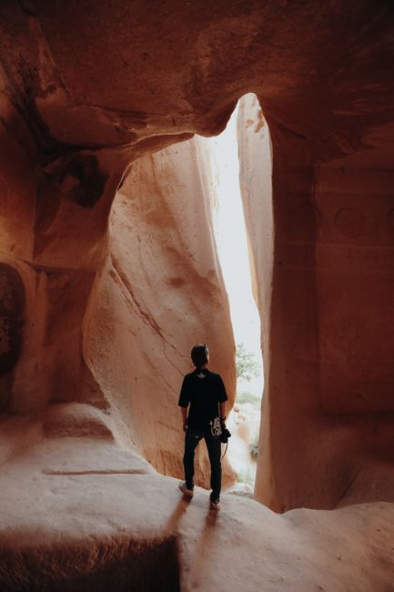 Person exploring a breathtaking sandstone cave with natural light streaming in.