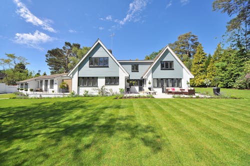 Free Modern family home exterior showcasing a large lawn and garden under a clear blue sky. Stock Photo