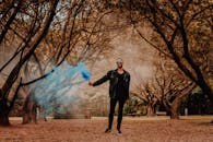 一名时尚男子在森林中手持蓝色烟雾弹摆姿势