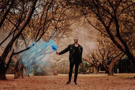 一名时尚男子在森林中手持蓝色烟雾弹摆姿势