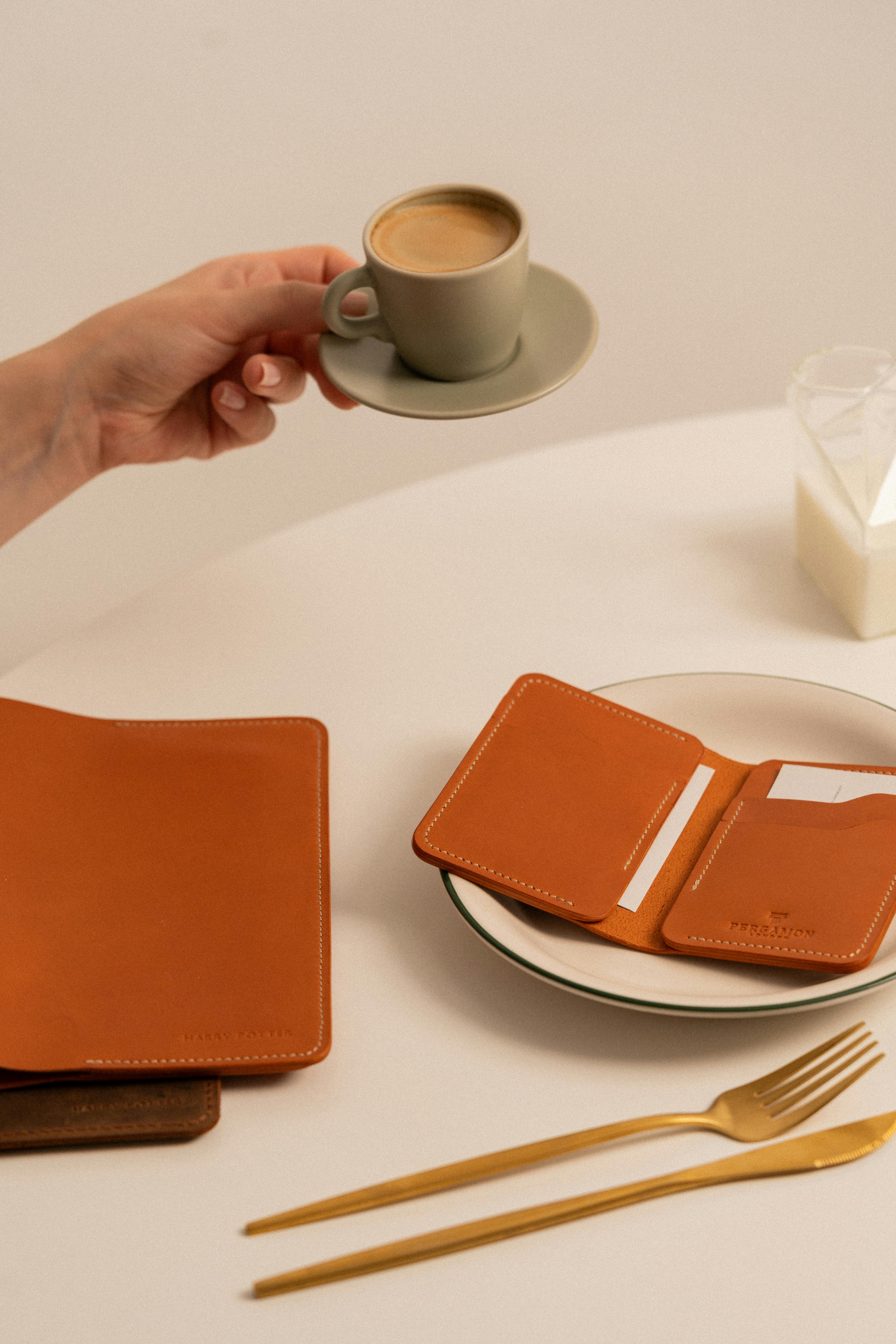 hand of a man holding a cup of coffee and a wallet on a plate