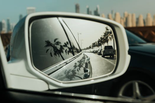 A travel scene with palm tree reflections in a car mirror along a Dubai road.