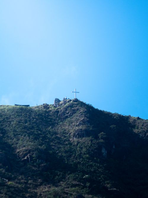 Free Cross atop a tranquil mountain ridge, symbolizing serenity under a clear blue sky. Stock Photo
