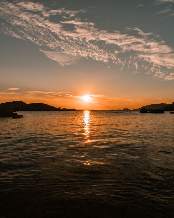 A sunset over the water with clouds and mountains · Free Stock Photo