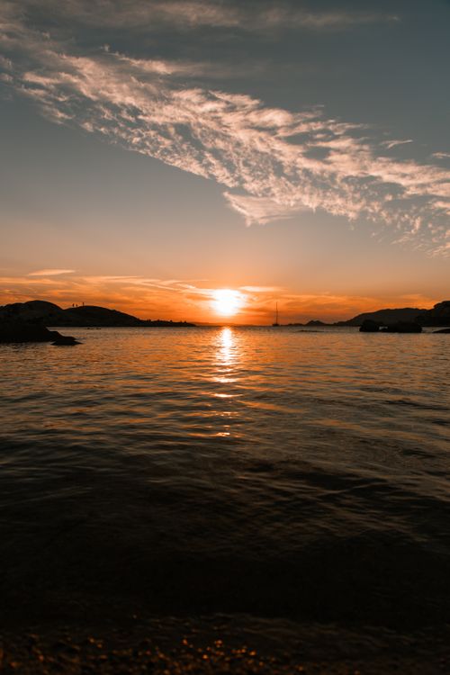 Free A stunning sunset over calm ocean waters with dramatic clouds and reflections. Stock Photo