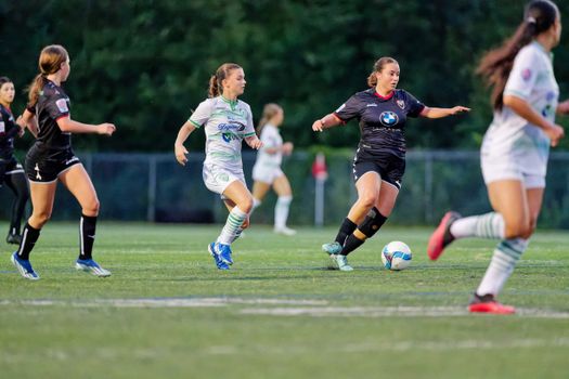Dynamic action shot of female soccer players in motion during a game on a grass field.