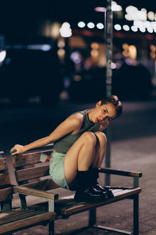 Free Woman sitting on a bench at night in an urban street scene, fashion-forward and relaxed. Stock Photo