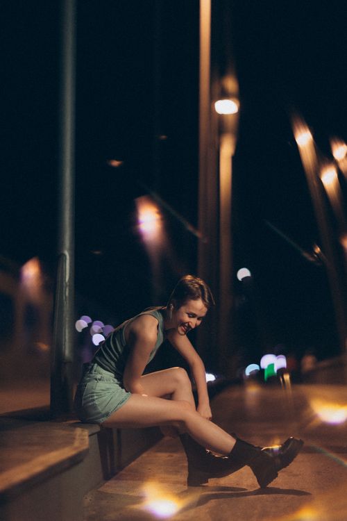 Free A young woman sitting on a bridge at night, under urban lights and a moody atmosphere. Stock Photo