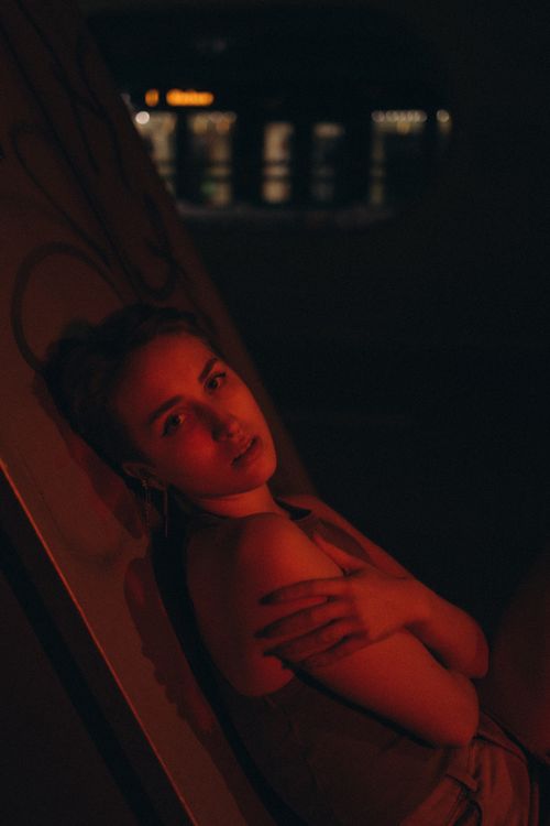 Free A dramatic, low-lit portrait of a young woman in an artistic indoor setting, creating a somber mood. Stock Photo