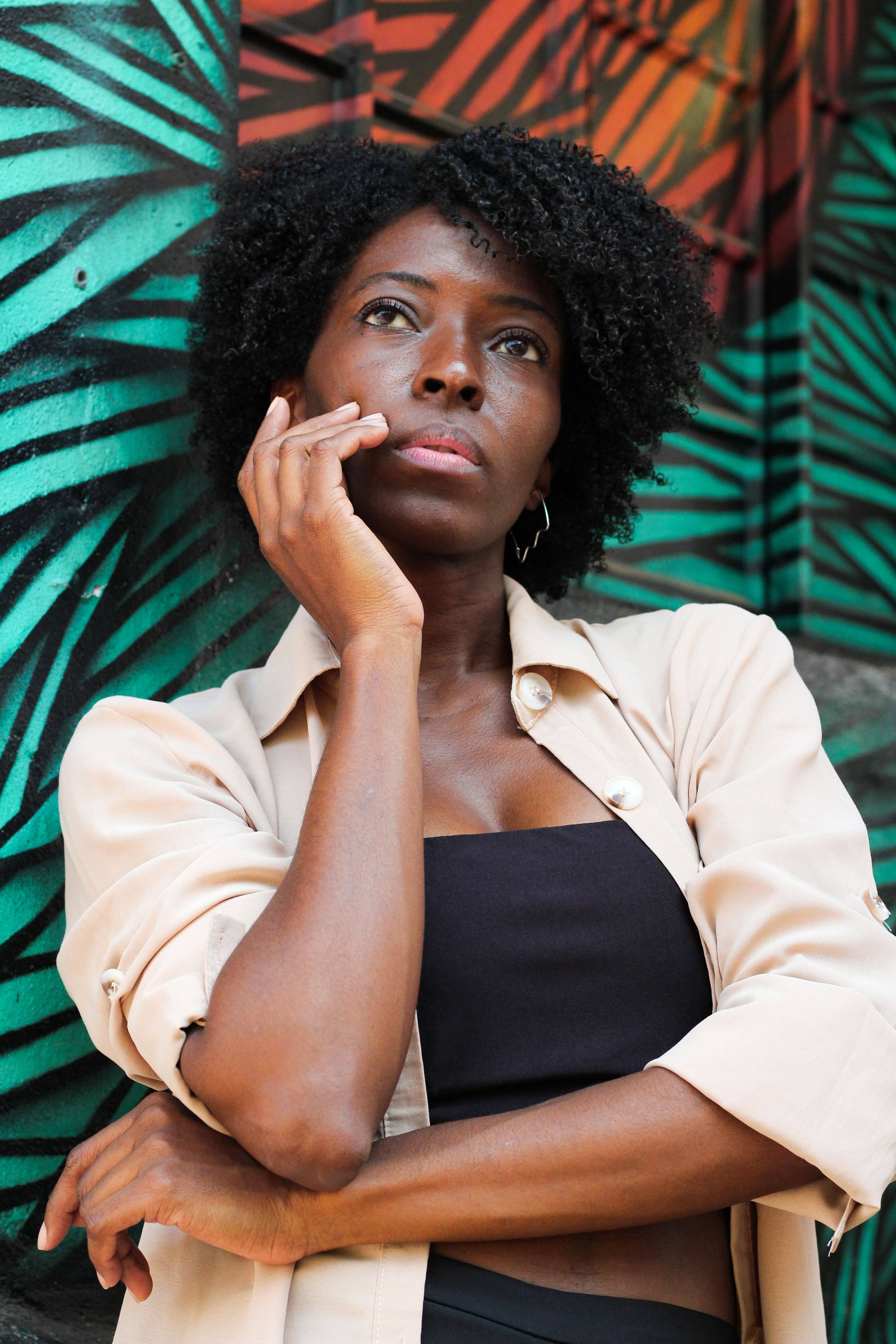 Portrait of a young woman standing against a vibrant mural, lost in thought.