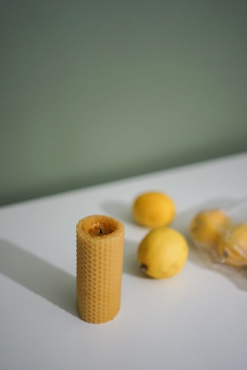 Free A simple still life featuring a beeswax candle and fresh lemons on a white surface. Stock Photo