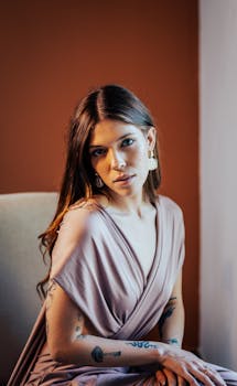 Portrait of a young woman in elegant attire sitting indoors with thoughtful gaze.