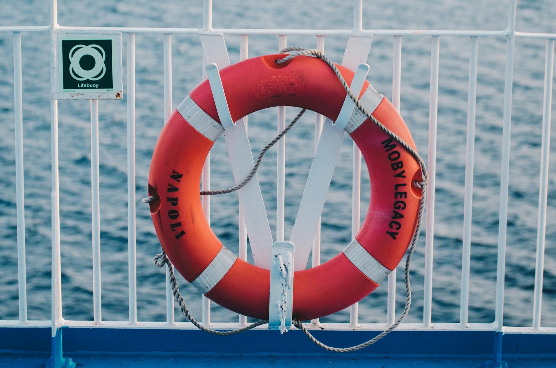 A bright red lifebuoy labeled 'Napoli' on a ship deck with ocean waves in the background.