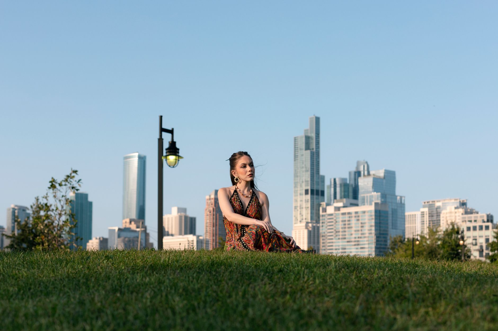 A young woman relaxes on a grassy hill with Chicago's skyline in the background.