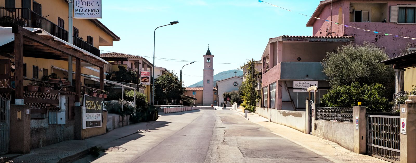 Sunny street scene in Porto San Giorgio, showcasing local architecture and a distant clock tower.