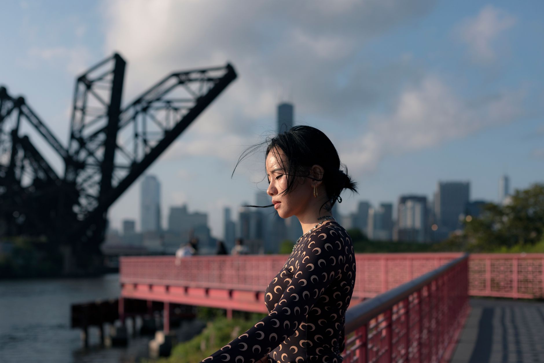 A woman posing by a Chicago river with the city skyline and bridge in the background at sunset.