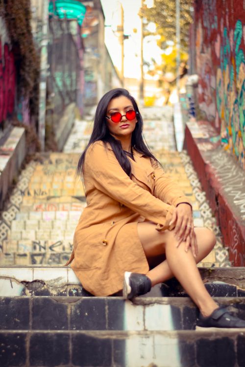 Free Stylish woman in red sunglasses sitting on graffiti-covered steps in an urban setting. Stock Photo