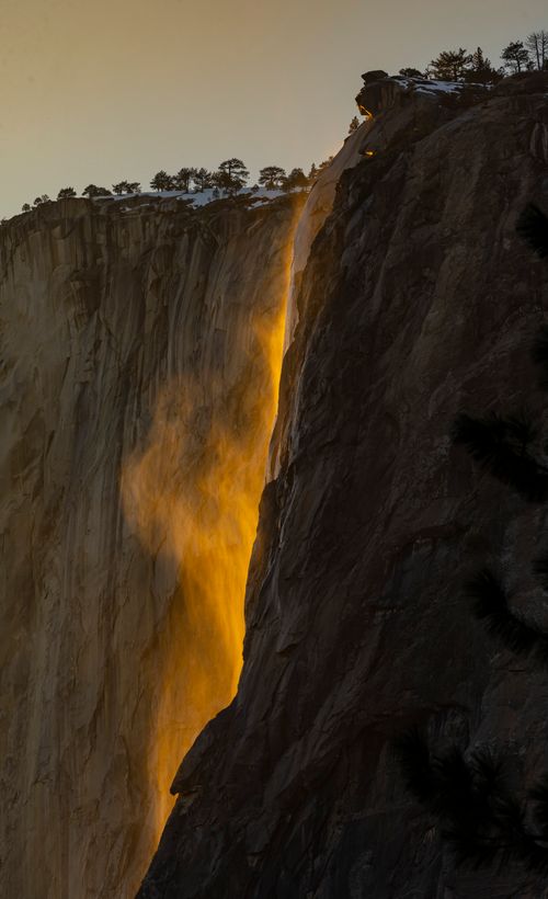 Free Waterfall glows like fire during sunset over a rugged cliff. Stock Photo