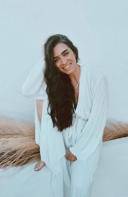 Free A smiling woman in a white dress sitting elegantly with long hair against a light blue backdrop. Stock Photo