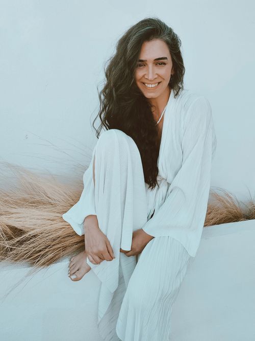 Free Portrait of a smiling woman with long hair in a flowing white dress, seated outdoors. Stock Photo