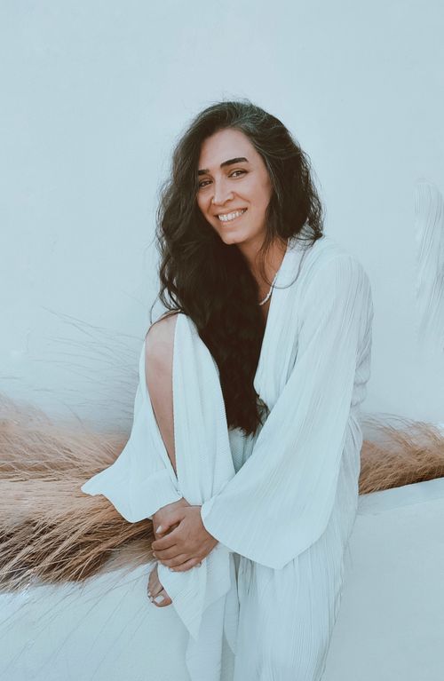 Free Happy brunette woman smiling and sitting gracefully in a white robe against a neutral background. Stock Photo