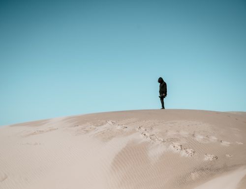 Free A lone individual wanders across sand dunes under a clear blue sky at Pismo Beach, California. Stock Photo