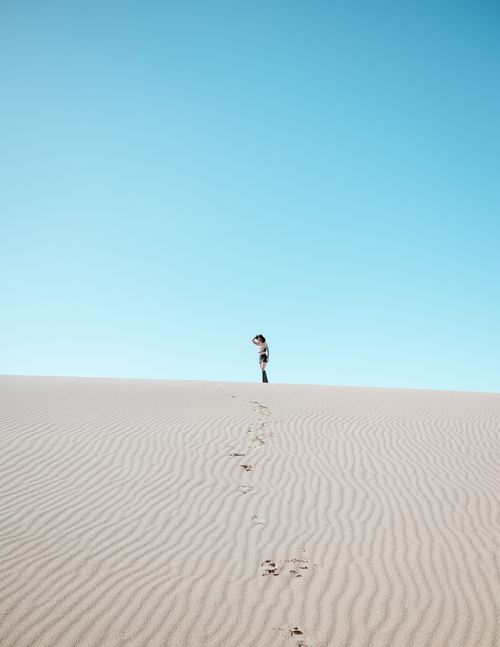 Free A solitary figure stands atop the sand dunes at Pismo Beach, California, with a clear blue sky overhead. Stock Photo