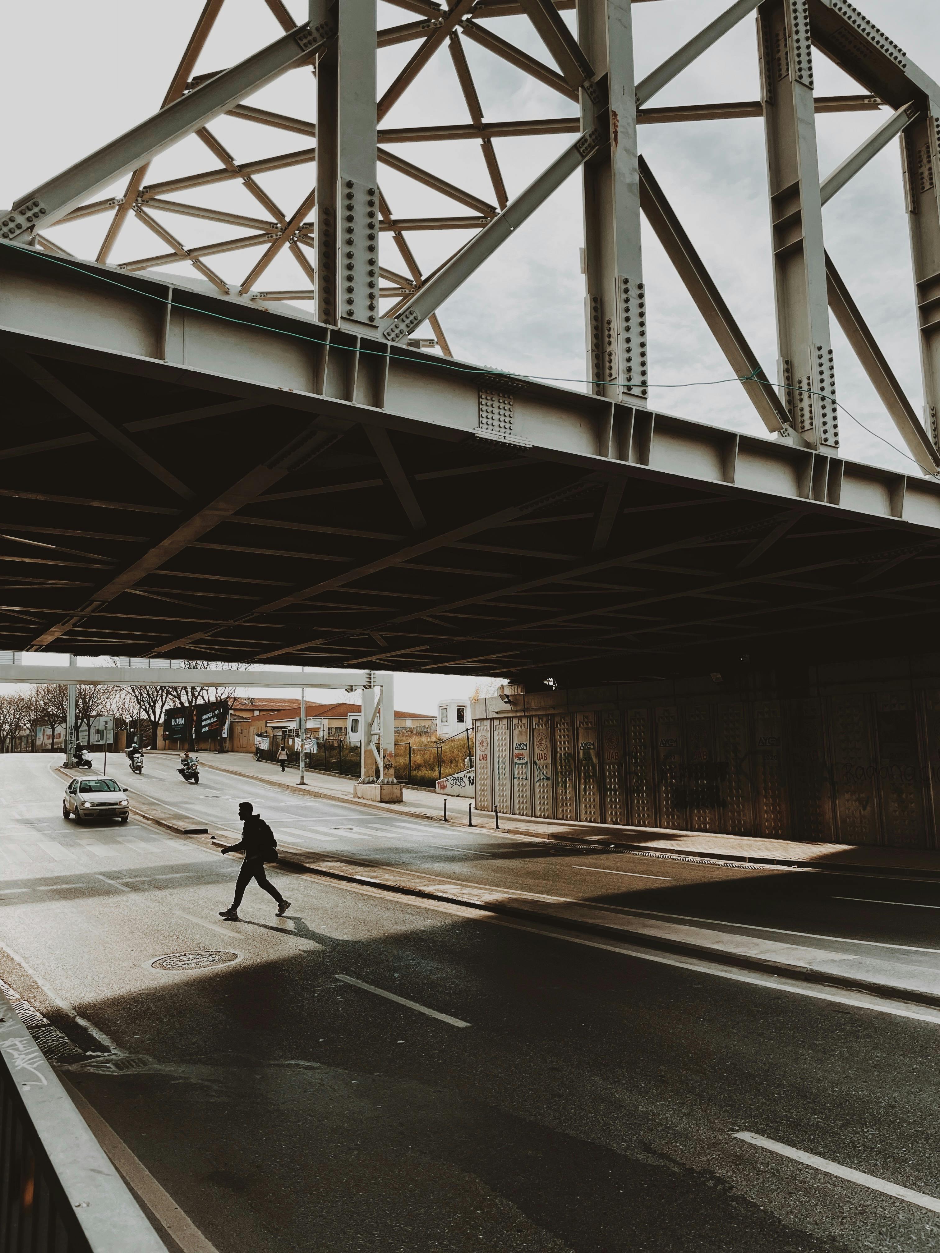 Person walking under bridge in İstanbul with cars passing by on a city street.
