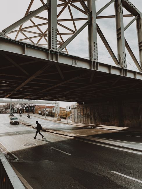 Person walking under bridge in İstanbul with cars passing by on a city street.