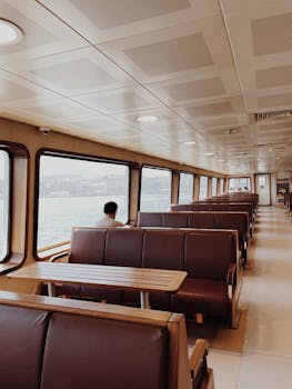Spacious ferry interior showcasing leather seating and large windows with waterfront view, ideal for travel and relaxation.