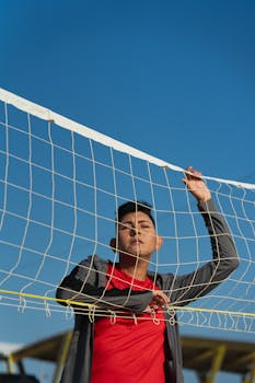 A young man in a red shirt stands confidently with a soccer net on a sunny day.