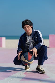 A young adult poses with a basketball on a vibrant beach court in Progreso, Mexico under a clear sky.