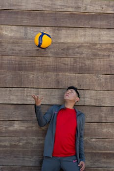 Dynamic portrait of a young man juggling a soccer ball against a rustic wooden wall.