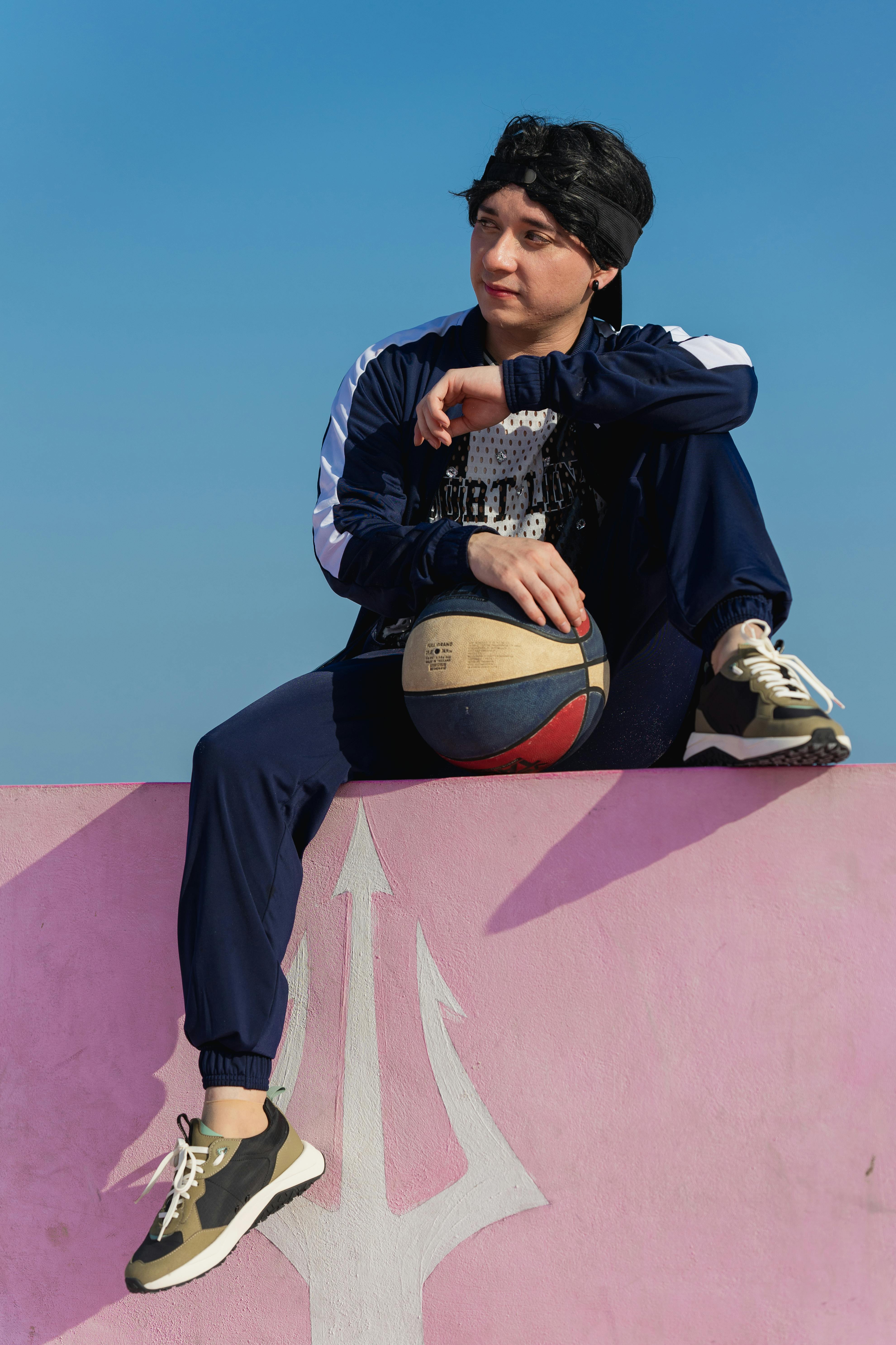 a young man sitting on top of a pink wall with a basketball