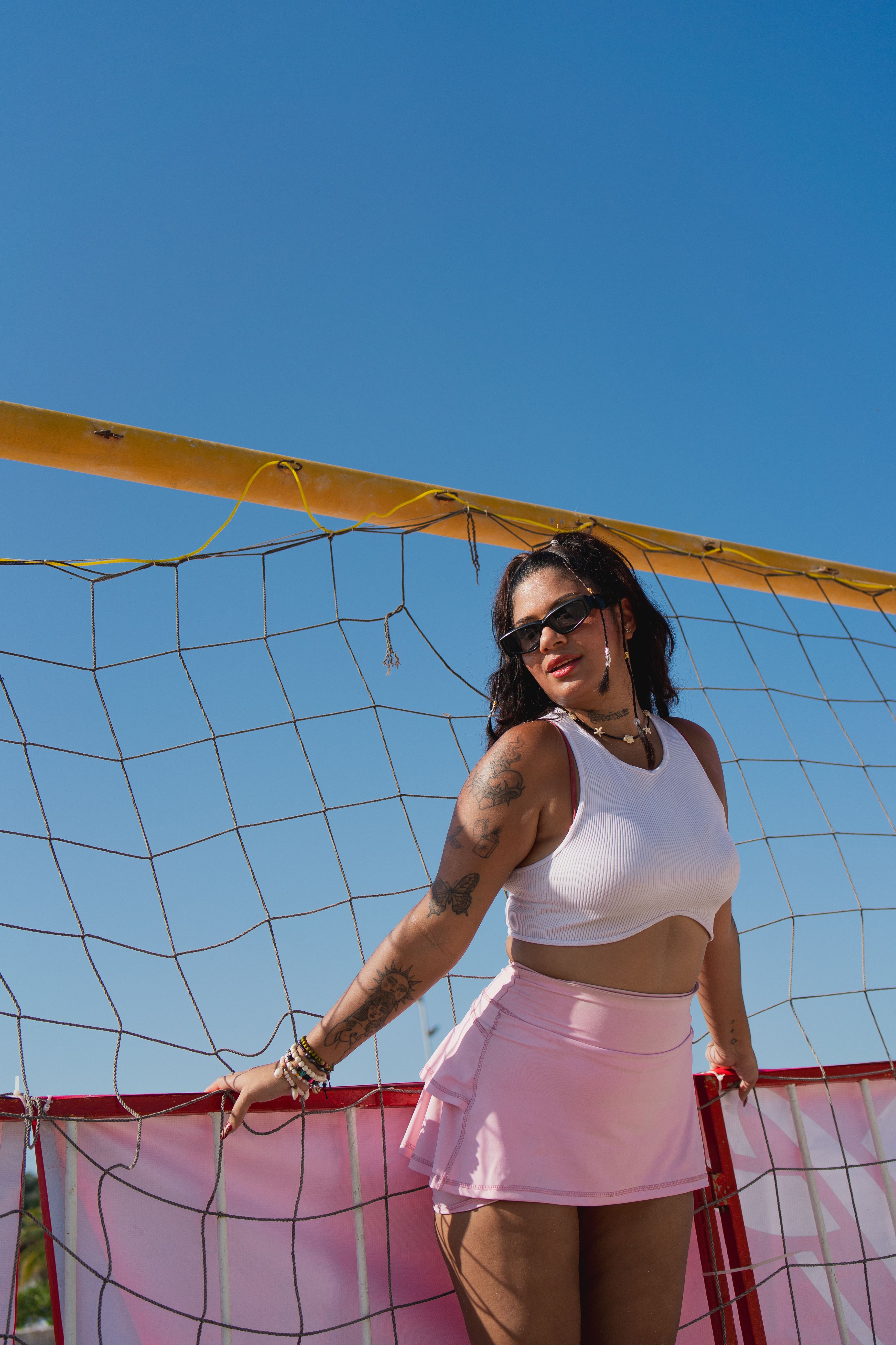 A woman in a white top and pink skirt posing near a volleyball net ...