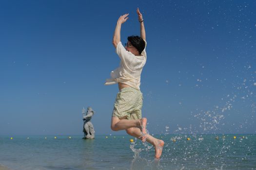 A person jumps joyfully on a sunny beach in Progreso, Mexico with a statue in the background.