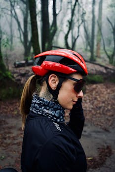 A woman in a red helmet cycling through a misty forest, blending adventure and serenity.