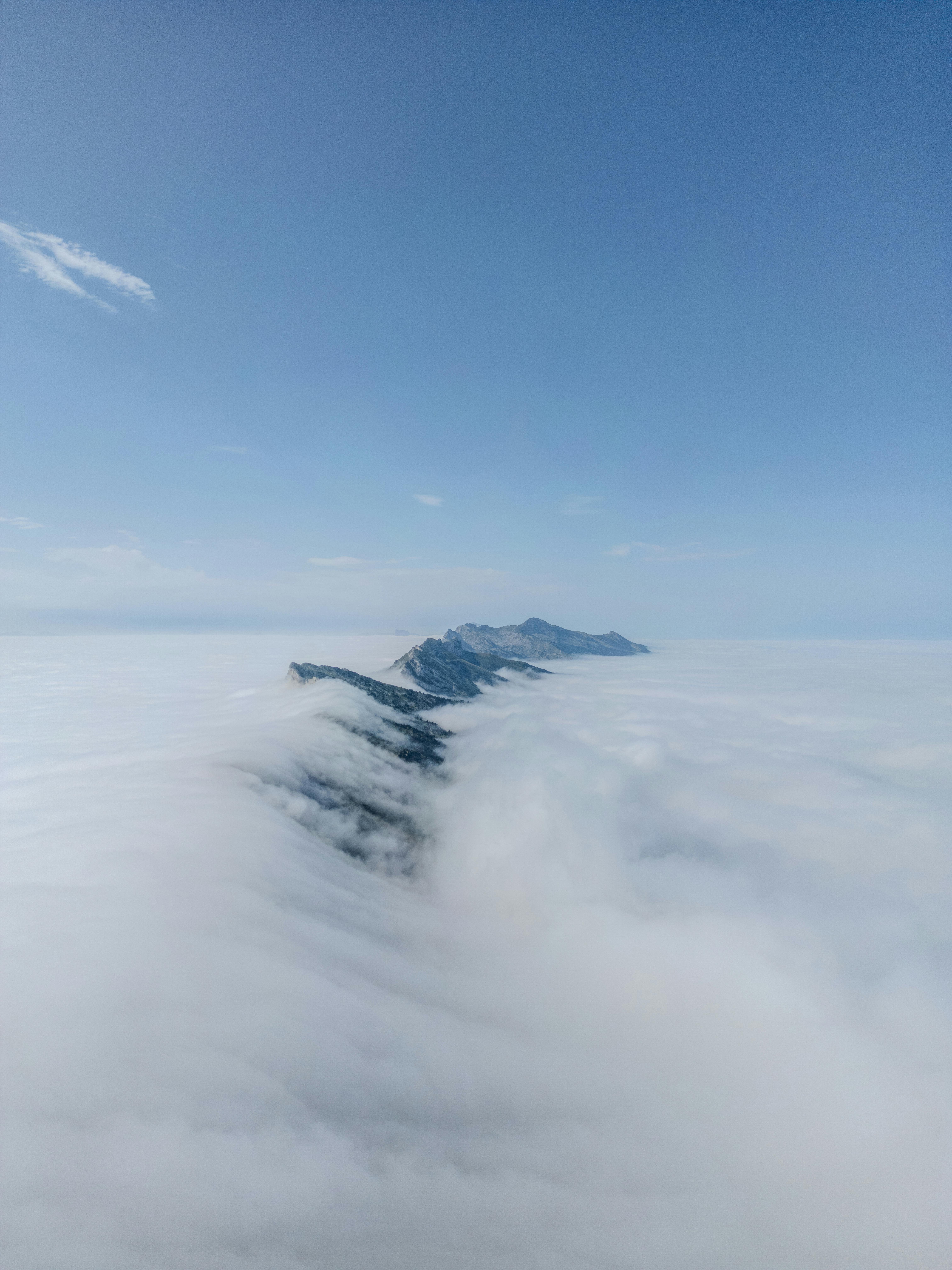 Stunning aerial shot of snow-covered Vercors Mountains under a clear blue sky, surrounded by clouds.
