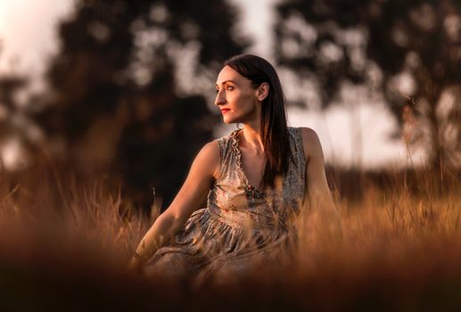 A woman in a floral dress sits in a sunny autumn field, basking in the warm sunset glow.